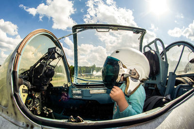 Side view of girl sitting in air vehicle against cloudy sky