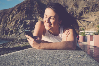 Smiling woman using mobile phone while lying down outdoors