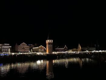 Illuminated buildings by river against sky at night