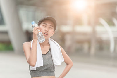 Young woman with towel wearing sports clothing while standing on footpath in city