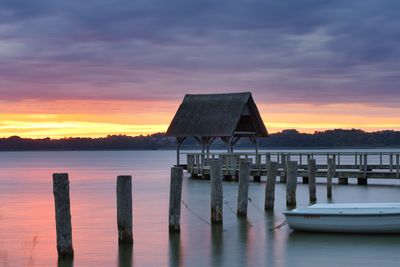 Wooden posts on pier over lake against sky during sunset