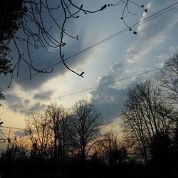 Low angle view of bare trees against cloudy sky