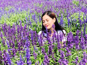 Portrait of a beautiful young woman with purple flowers on field