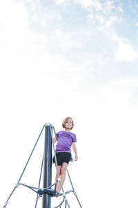Low angle view of girl standing on outdoor play equipment against cloudy sky at playground