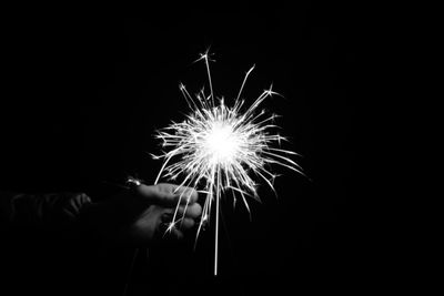 Close-up of hand holding illuminated fireworks against sky at night
