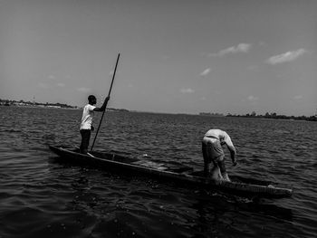 Rear view of man fishing in sea against sky