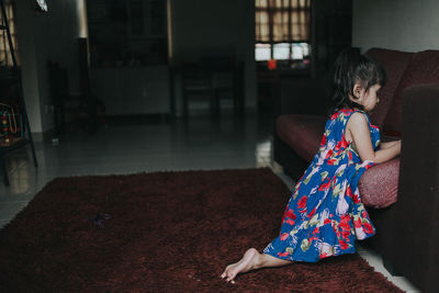 Side view of girl kneeling on carpet in living room at home