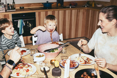 Playful kids having meal with parents while sitting at dining table in home