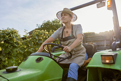 Farmer wearing straw hat driving tractor in vineyard