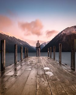 Rear view of woman standing on pier over lake against sky during sunset