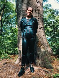 Portrait of smiling woman standing by tree trunk in forest