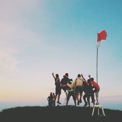 Low angle view of friends jumping on hill by indonesian flag at sunset