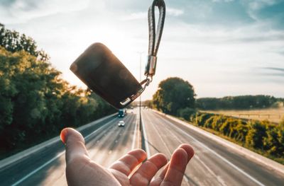 Hand holding glass of road against sky