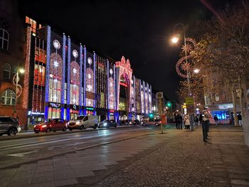 Illuminated city street by buildings at night