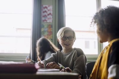 Happy boy talking with friend while sitting in classroom