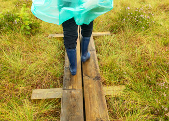 Wooden footbridge in the swamp, human feet in rubber boots, swamp vegetation