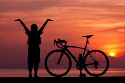 Silhouette man standing by bicycle against sky during sunset