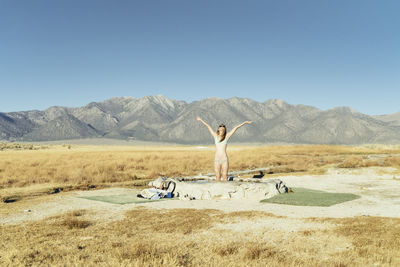 Happy woman standing in swimming pool on field by mountains against clear sky