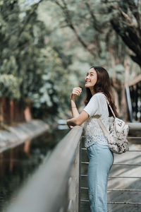 Side view of young woman standing against trees