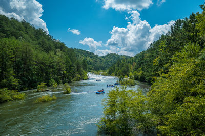 Groups of people in large rafts going whitewater rafting down the river approaching the rapids 