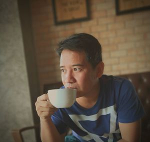 Thoughtful man drinking coffee while sitting against wall at home