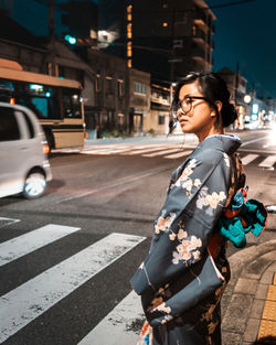 Side view of young woman in traditional clothing waiting at zebra crossing in city