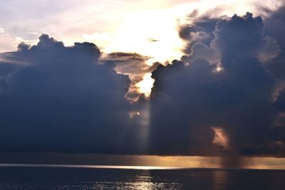 Sunlight streaming through clouds in sea during sunset