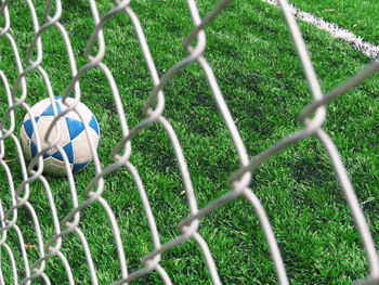 Soccer ball on field seen through chainlink fence