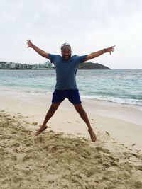 Portrait of happy man with arms outstretched jumping at beach against sky