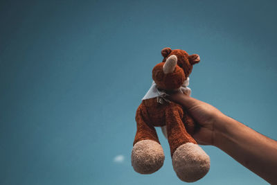 Cropped hand of man holding stuffed toy against blue background