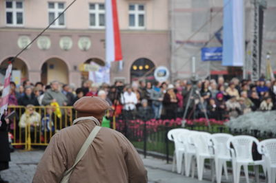 Rear view of man walking on street by crowd against building