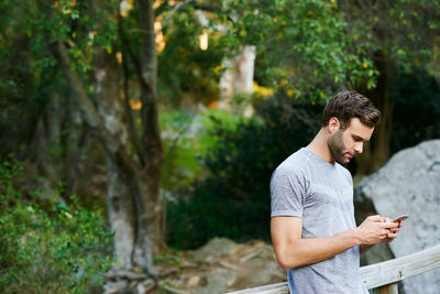 Young man looking away while standing against trees