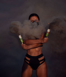 Woman in lingerie holding distress flare outdoors
