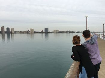 Rear view of couple standing on pier on sea against sky