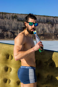 Full length of shirtless man drinking water