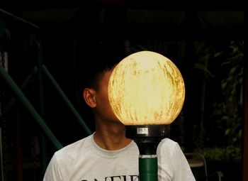 Close-up of man by illuminated lamp post at night