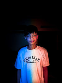 Portrait of young man standing against black background