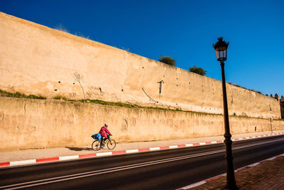 Man riding bicycle on sidewalk by wall