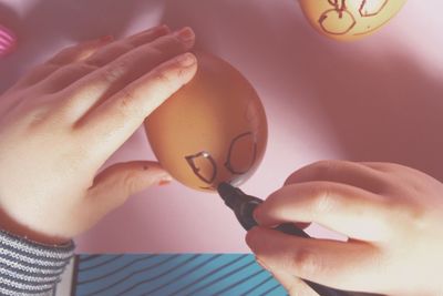 Cropped image of person drawing face on egg at home