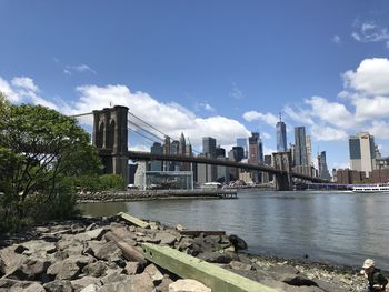 Bridge over river by buildings in city against sky