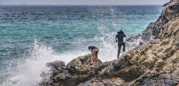 Rear view of men on rock formation fishing in sea