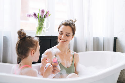 Young mother woman and little tween girl daughter having fun in bath with foam at home
