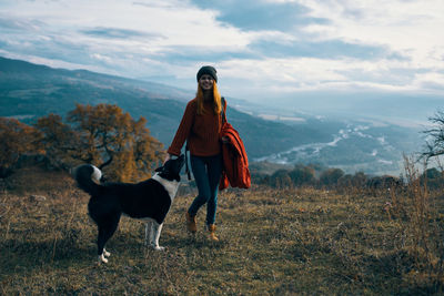 Woman with dog standing on mountain against sky