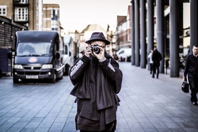 Man wearing hat photographing while standing in city