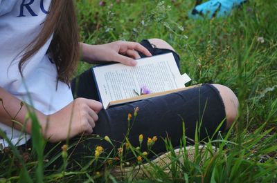 Cropped image of woman reading book while sitting at grassy field