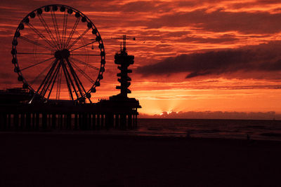 Silhouette ferris wheel at beach during sunset