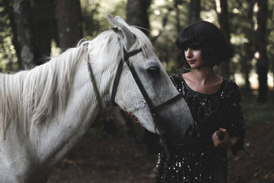 Young woman standing by horse in forest