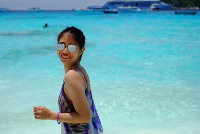 Portrait of young woman wearing sunglasses standing at beach