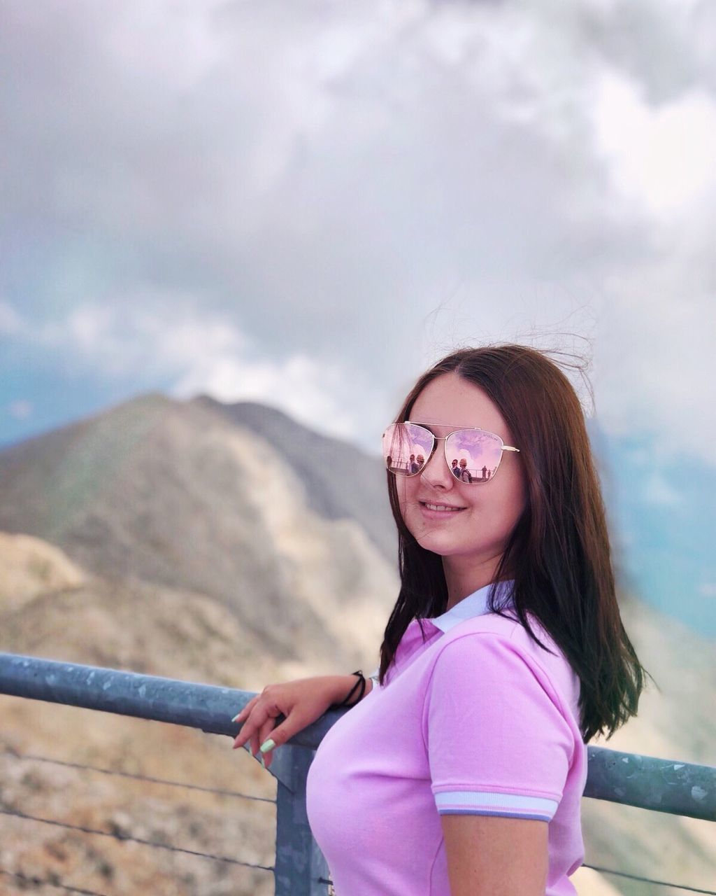 PORTRAIT OF A SMILING YOUNG WOMAN STANDING ON MOUNTAIN