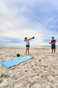 Fitness instructor assisting woman in exercising at beach
